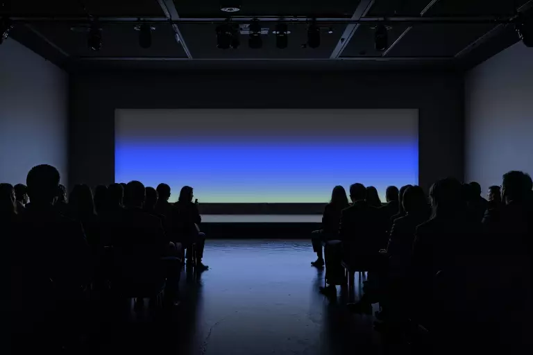 Publikum im abgedunkelten Saal blickt auf eine leuchtende Leinwand