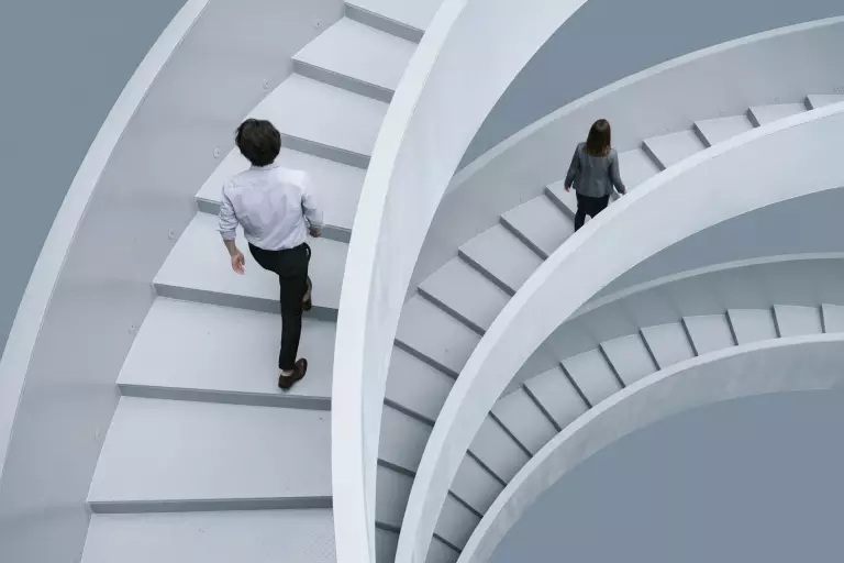Zwei Personen steigen eine weiße Wendeltreppe hinauf, von oben gesehen